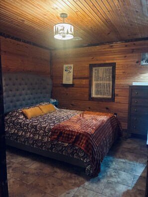 A bedroom with a bed, a dresser, a wall-mounted lamp, and a framed picture. - The Killabrew Cabin Hot Tub & Country Escape (Hulbert)
