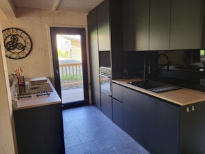A modern kitchen with dark cabinetry, a wooden countertop, and a clock on the wall. - One-bedroom Cabin (Sankt Georgen am Kreischberg)