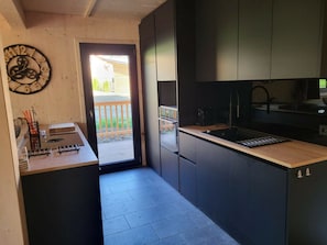 A modern kitchen with dark cabinetry, a wooden countertop, and a clock on the wall. - One-bedroom Cabin (Sankt Georgen am Kreischberg)