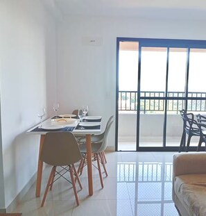 A dining area with a table set for two, a sofa, and a sliding glass door leading to an outdoor balcony. - 2-bedroom apartment near 44th Street | Swimming pool | Garage | Air conditioning (Goiânia)