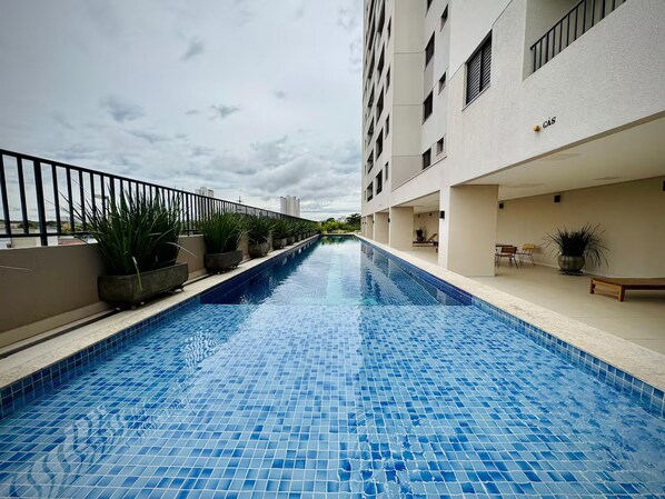 A swimming pool with a tiled floor, surrounded by a building with balconies and potted plants. - 2-bedroom apartment near 44th Street | Swimming pool | Garage | Air conditioning (Goiânia)