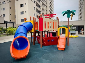 An outdoor play area with a slide, climbing structures, and a palm tree decoration. - 2-bedroom apartment near 44th Street | Swimming pool | Garage | Air conditioning (Goiânia)