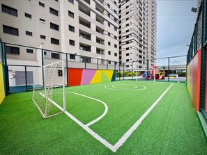 An indoor soccer field with a goalpost, surrounded by a fence, and adjacent to a multi-story building. - 2-bedroom apartment near 44th Street | Swimming pool | Garage | Air conditioning (Goiânia)
