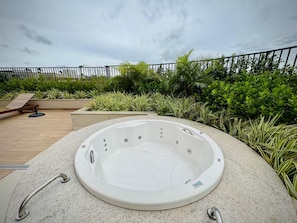 A hot tub in an outdoor setting with a wooden deck and lush greenery. - 2-bedroom apartment near 44th Street | Swimming pool | Garage | Air conditioning (Goiânia)