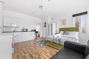 Une chambre à coucher moderne avec une tête de lit verte, un couvre-lit gris et un canapé noir.
