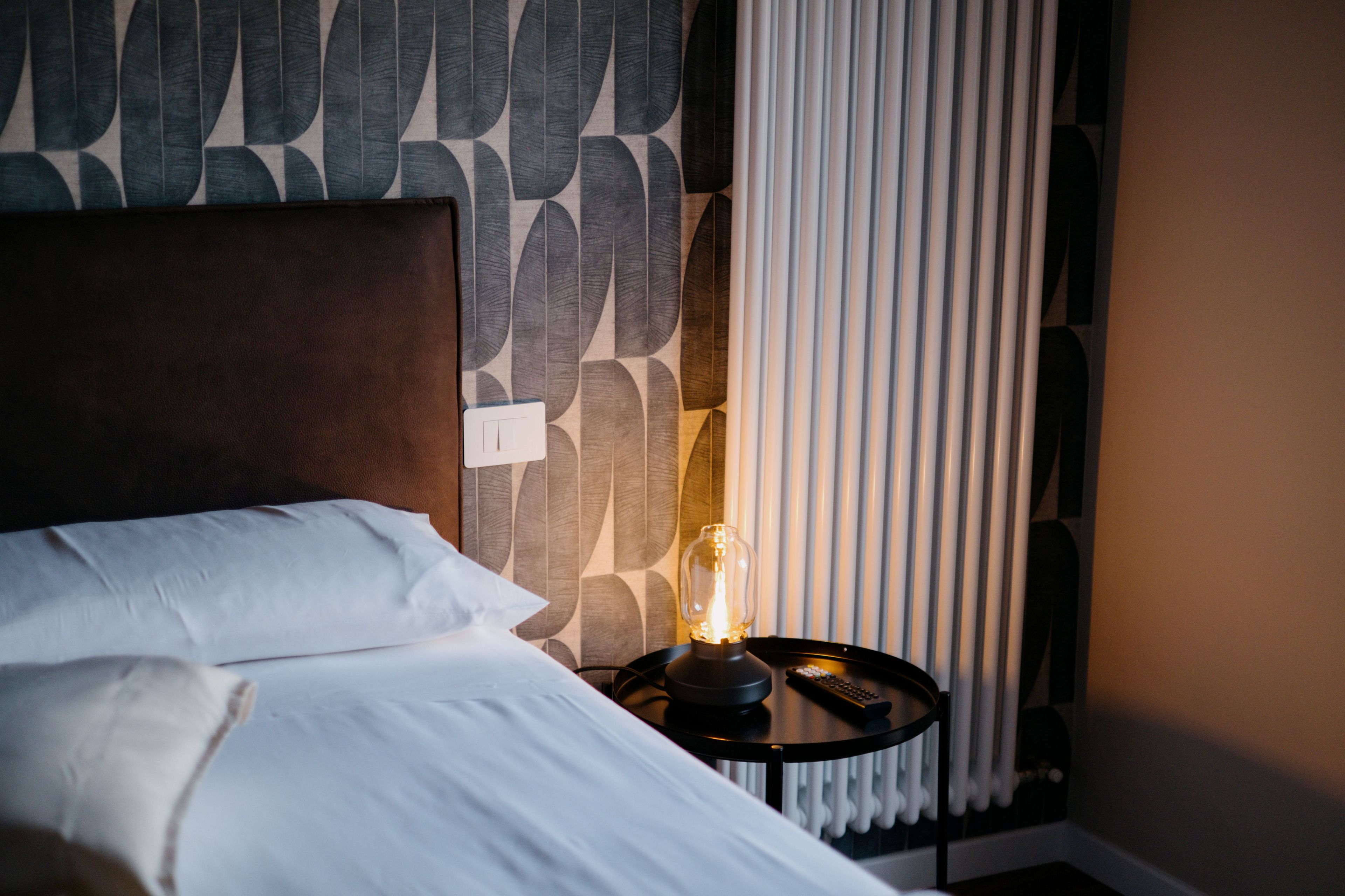 A neatly made bed with white linens, a modern headboard, and a bedside table with a lamp and remote control.