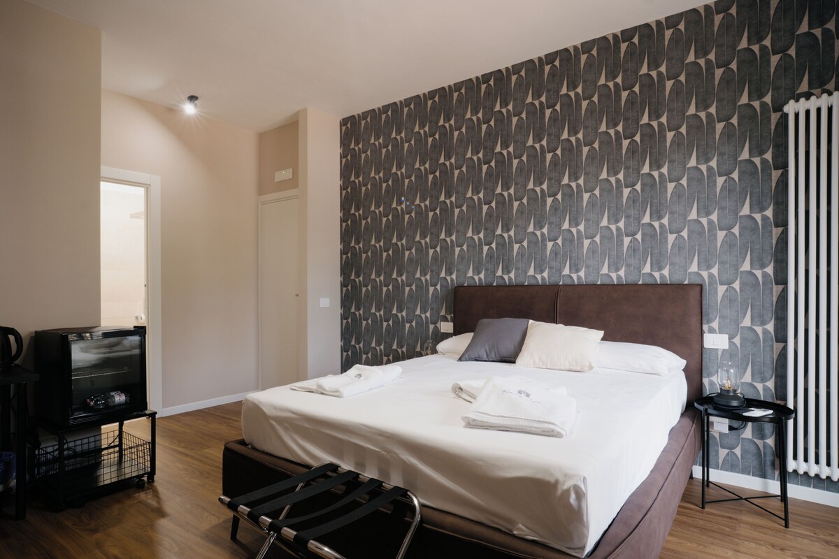 Een hotelkamer met een groot bed, een hoofdbord, een nachtkastje, een radiator en een kledingkast.