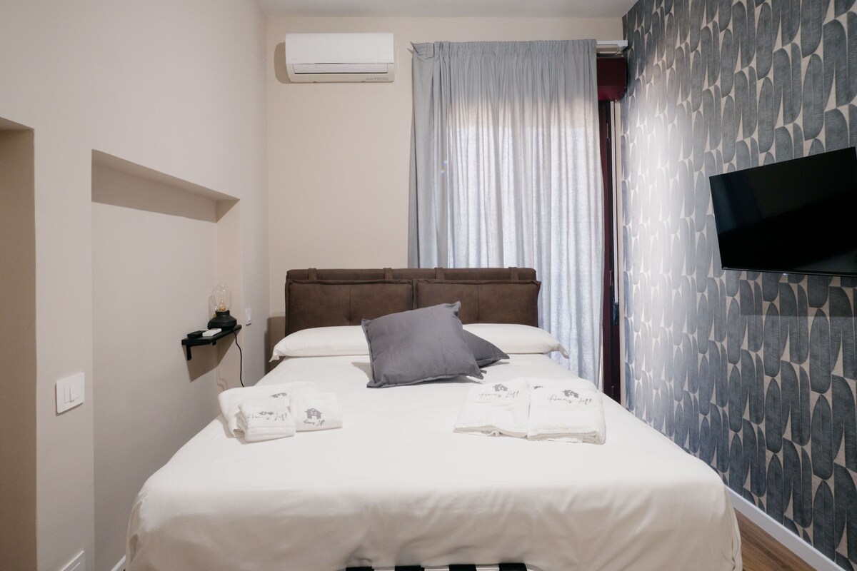 Een hotelkamer met een bed, een flatscreen televisie, een wandairconditioner en een raam met gordijnen.