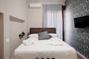 Een hotelkamer met een bed, een flatscreen televisie, een wandairconditioner en een raam met gordijnen.