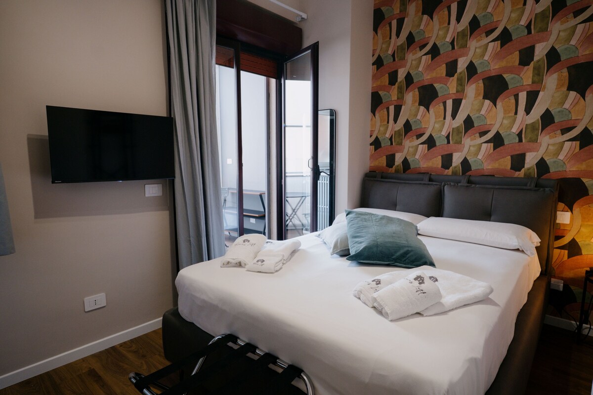 Een hotelkamer met een bed, een flatscreen televisie aan de muur, een raam met gordijnen en een behang met een patroon.