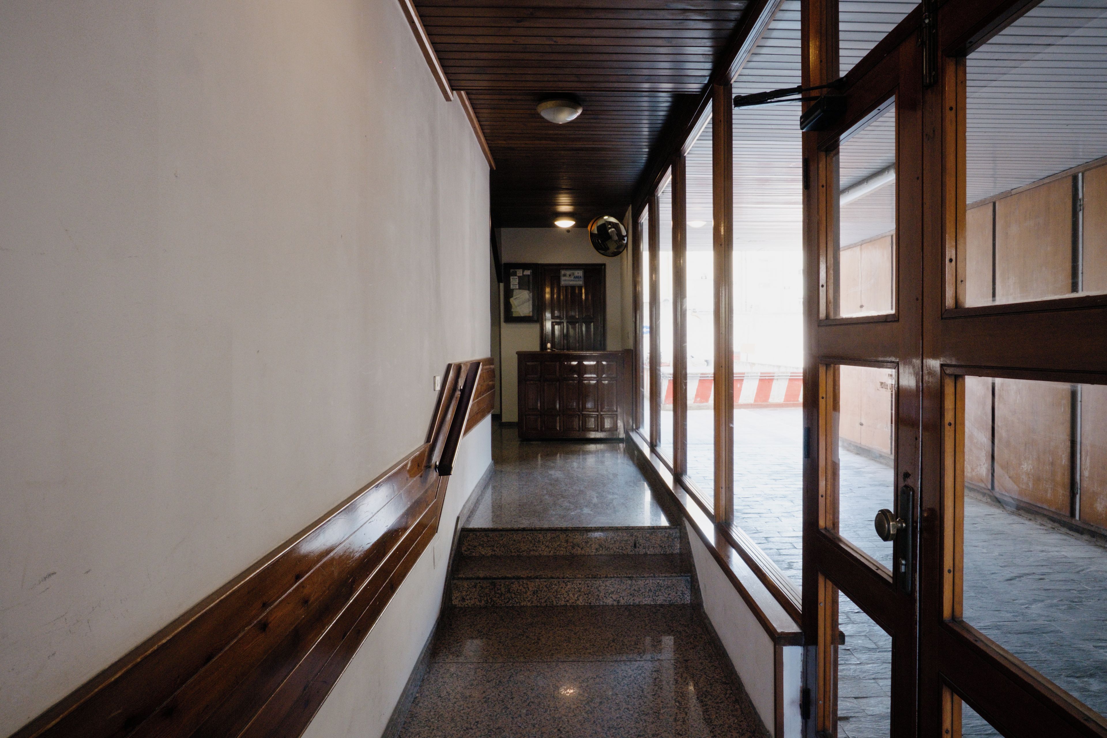 A corridor with wooden paneling, a staircase, and a door leading outside.