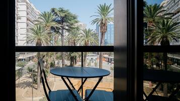 A balcony with a table and chairs, overlooking a street with palm trees and buildings.
