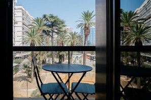 Een balkon met een tafel en stoelen, met uitzicht op een straat met palmbomen en gebouwen.