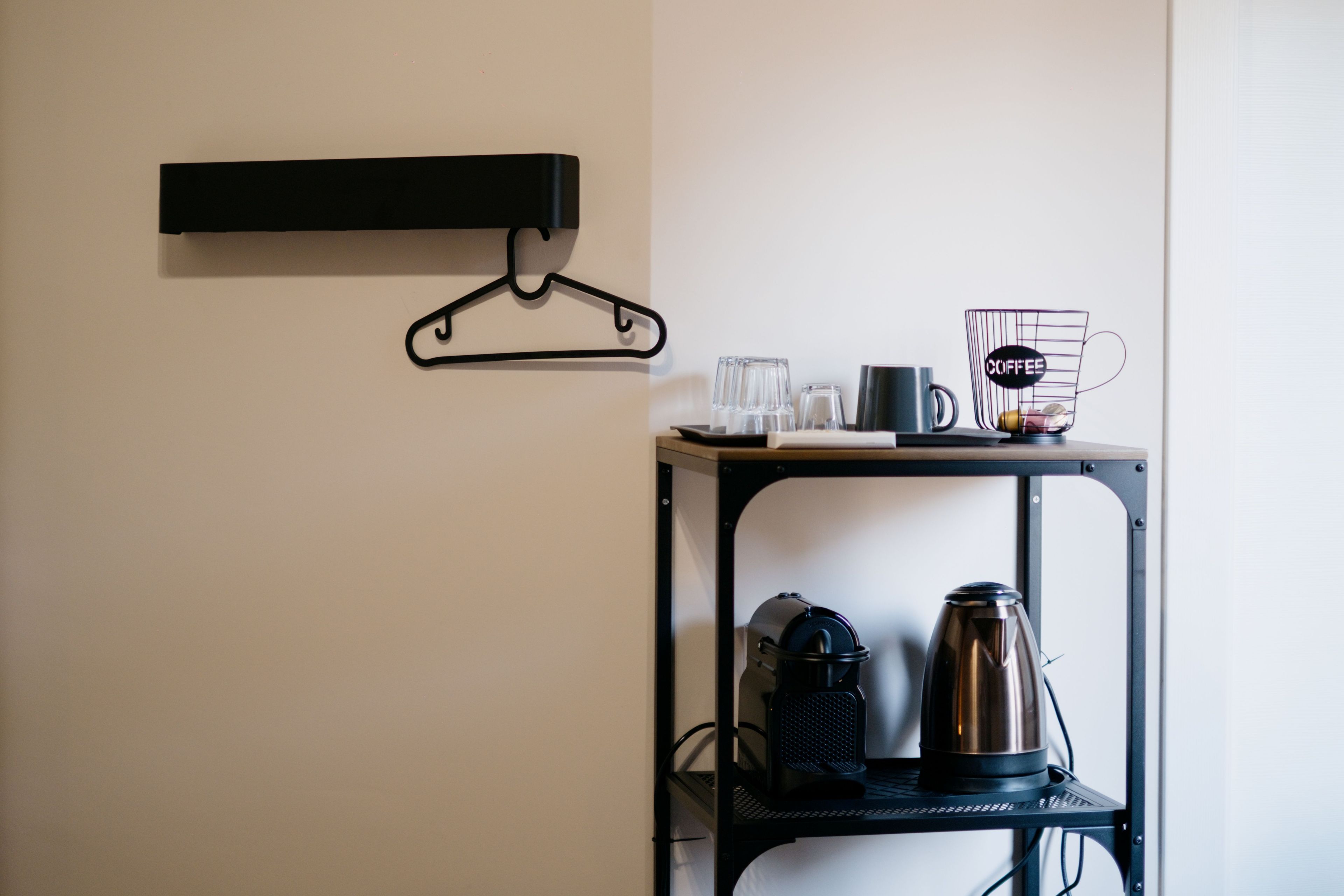A kitchenette with a coffee maker, a kettle, and a mug on a black metal shelf.