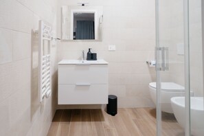 Een moderne badkamer met een wit wastafelmeubel, een spiegel, een zwarte prullenbak en een toilet.
