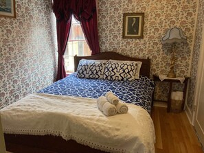Un dormitori amb un edredó estampat, un panell de fusta al capçal del llit, un quadre encimbellat a la paret, una làmpada de nit i una tovallola arremolinada damunt del llit.