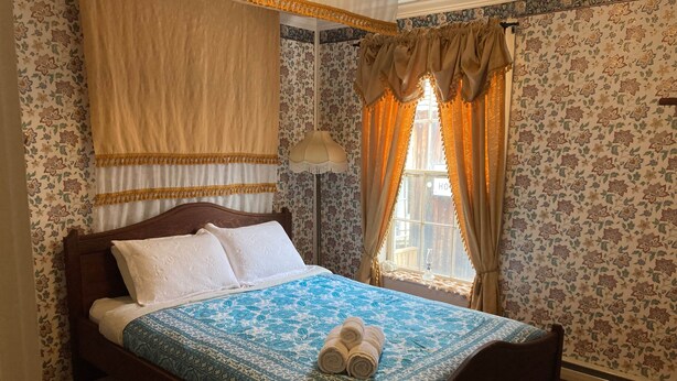 Cama bem arrumada com colcha estampada, um par de toalhas enroladas e cabeceira de madeira.