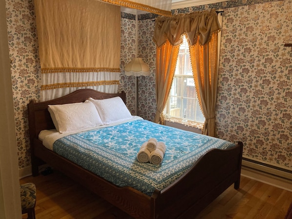 A neatly made bed with a patterned bedspread, a pair of rolled towels, and a wooden headboard. - Room 3 - St. George Hotel (Barkerville)