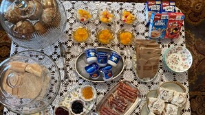Uma mesa com diversos alimentos e acompanhamentos, incluindo doces, frutas, iogurte e salgadinhos embalados.