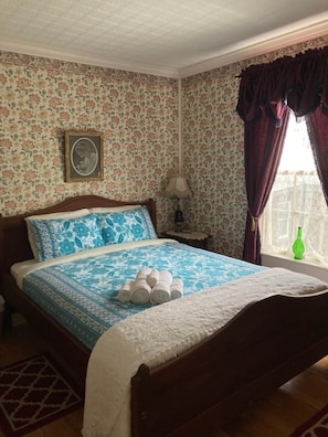Un dormitorio con cama, mesita de noche, lámpara, ventana con cortinas y un papel tapiz floral.