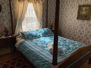 A four-poster bed with a floral-patterned bedspread, a wooden headboard, and a nightstand with a lamp.