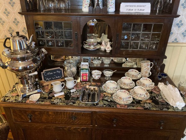 A continental breakfast setup with a coffee station, tea service, and a variety of teacups and saucers.