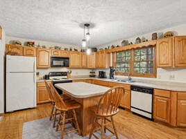 Cocina con armarios de madera, un refrigerador, estufa, pileta y ventana con vista a árboles.