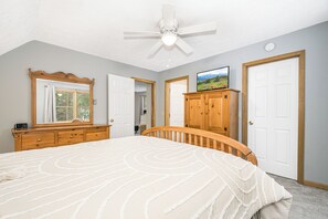 A bedroom with a bed, a television on a wooden cabinet, a ceiling fan, and two doors. - On A Whim (Swanton)