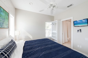 A bedroom with a bed, a ceiling fan, a TV, and a bathroom door. - No Agenda Hacienda (Port Aransas)