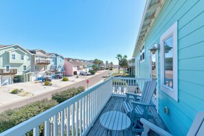 A residential street with colorful houses, a stop sign, and a balcony with outdoor furniture. - No Agenda Hacienda (Port Aransas)