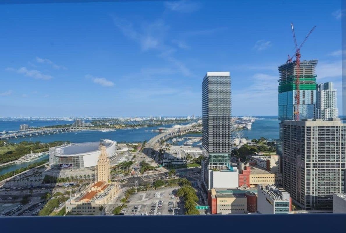 Un paisaje urbano con un rascacielos en construcción, un edificio histórico y una zona frente al mar.
