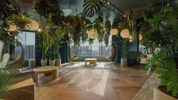 Amplia habitación con techo alto, piso de madera y una variedad de plantas en macetas. Hay dos mesas redondas y un área de estar con sillas.