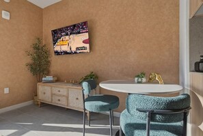 Un comedor con una mesa redonda, dos sillas, un aparador con objetos decorativos y un cuadro colgado en la pared.