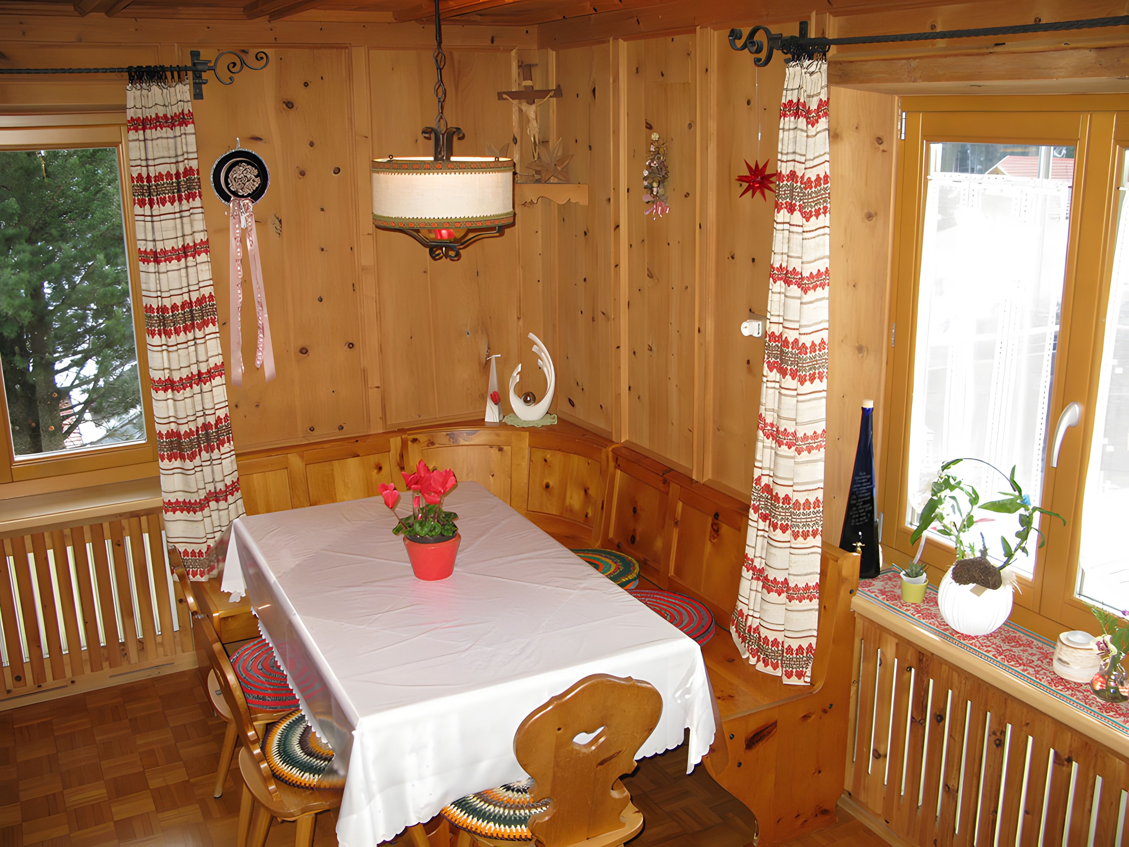 A wooden interior with a table set for dining, a bench, and a window with curtains.