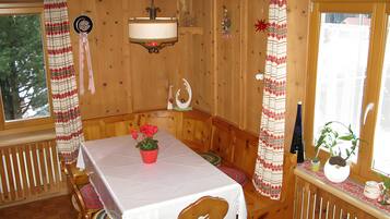 A wooden interior with a table set for dining, a bench, and a window with curtains.