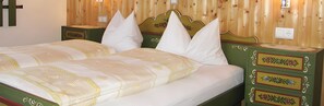 Un lit avec une couvre-lit à motifs floraux et plusieurs oreillers, une tête de lit en bois et une table de chevet verte avec des tiroirs.