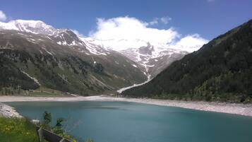 Ein Bergsee mit blauem Himmel, umgeben von bewaldeten Hängen und schneebedeckten Gipfeln.