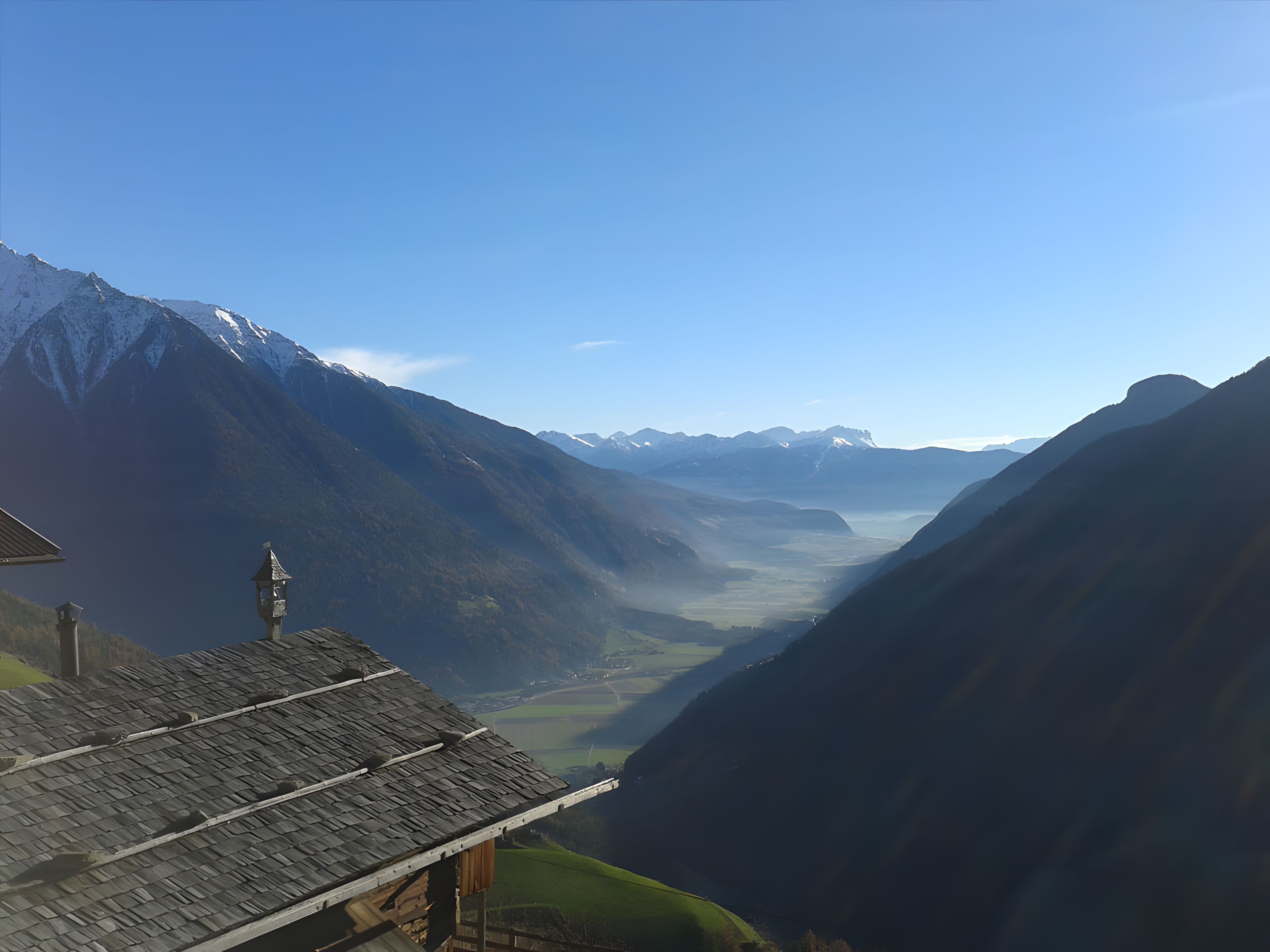 A mountain landscape with a valley, a building with a sloped roof, and a bell tower.