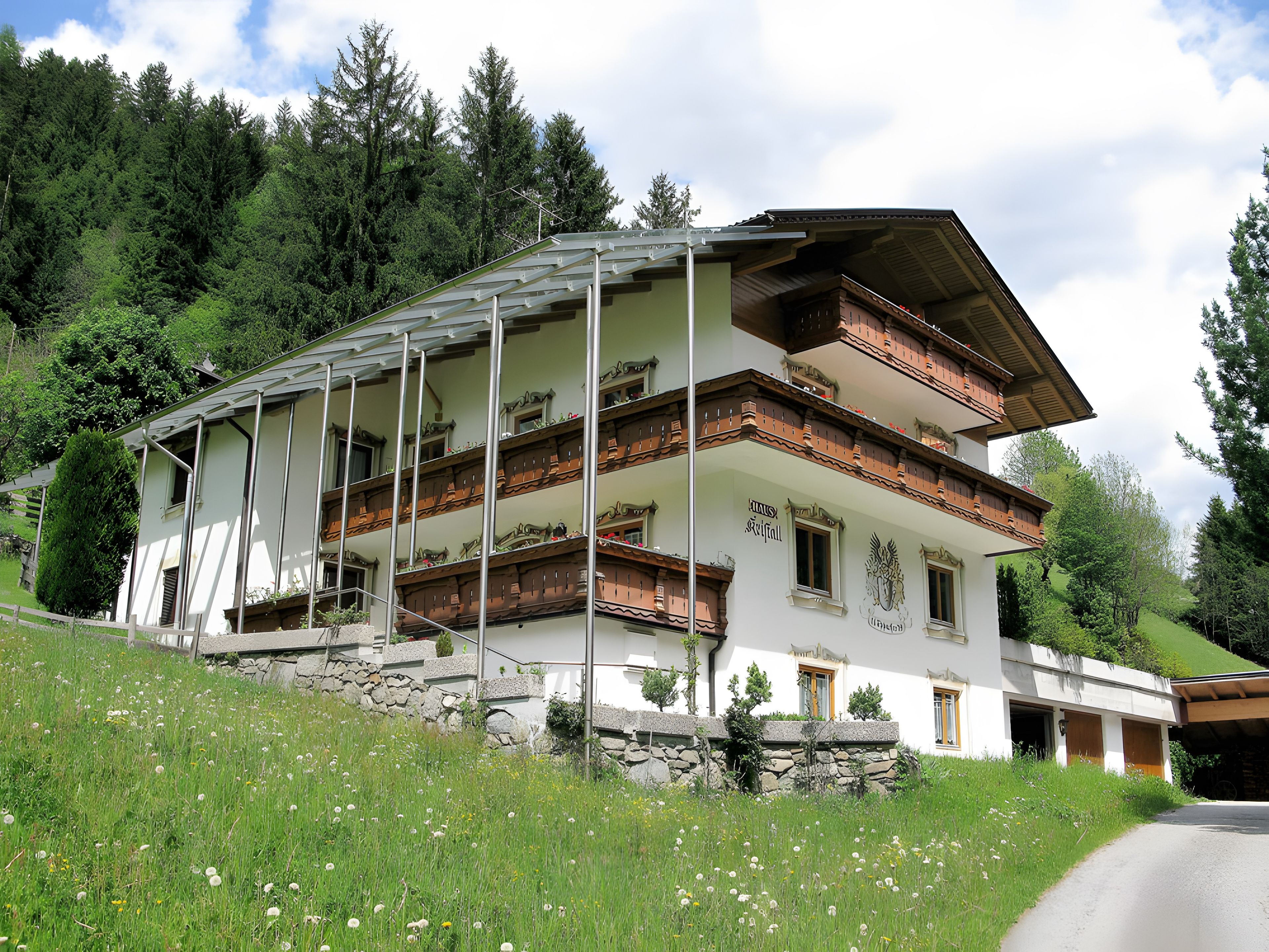 Ein mehrstöckiges Chalet mit Balkonen, gelegen an einem Hang mit einer Steinschmalseite und einem Rasen im Vordergrund.