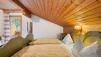Une pièce avec un plafond en pente, un lit doté d’une tête de lit, une fenêtre donnant sur des arbres et un luminaire fixé au mur.