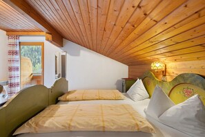 A room with a sloped ceiling, a bed with a headboard, a window with a view of trees, and a wall-mounted light fixture.