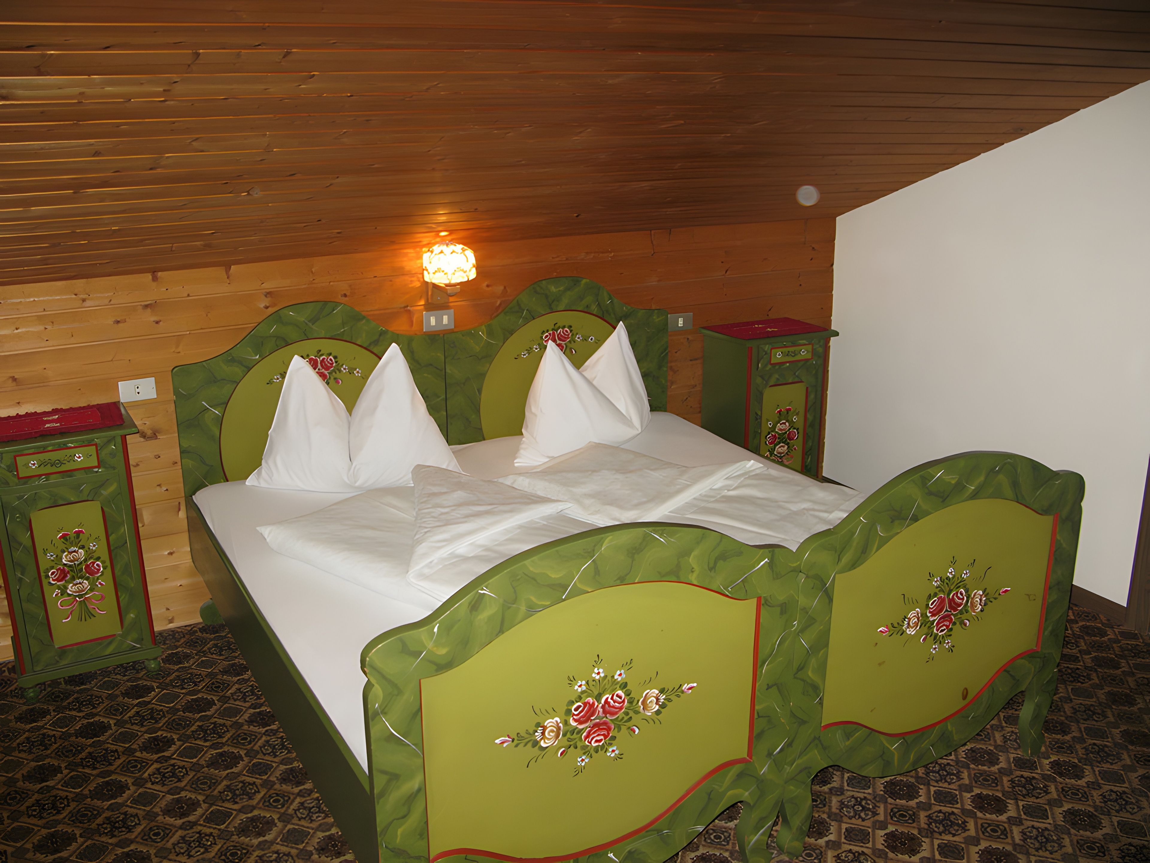 Ein Zimmer mit Holzboden, einem Bett mit grünen Kopfteilen, weißer Bettwäsche und einem Nachttisch mit einer roten Ablage.