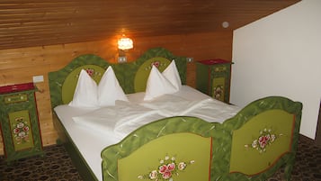 Ein Zimmer mit Holzboden, einem Bett mit grünen Kopfteilen, weißer Bettwäsche und einem Nachttisch mit einer roten Ablage.
