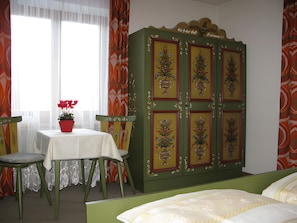 A room with a bed, a table with a potted plant, and a green cabinet with decorative panels.