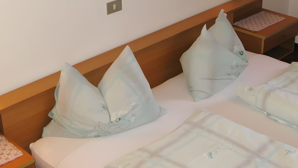 A hotel room with a wooden headboard, two pillows, a bedside table with a lamp, and a bed with a patterned bedspread. - Apartment '1' with Mountain View, Shared Garden and Wi-Fi (Selva dei Molini)