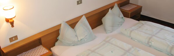 Une chambre d’hôtel avec une tête de lit en bois, deux oreillers, une table de chevet avec une lampe et un lit recouvert d’une couvre-lit à motifs.