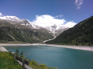 Un lac de montagne aux eaux limpides, sous un ciel dégagé, entouré de pentes boisées et de sommets enneigés.