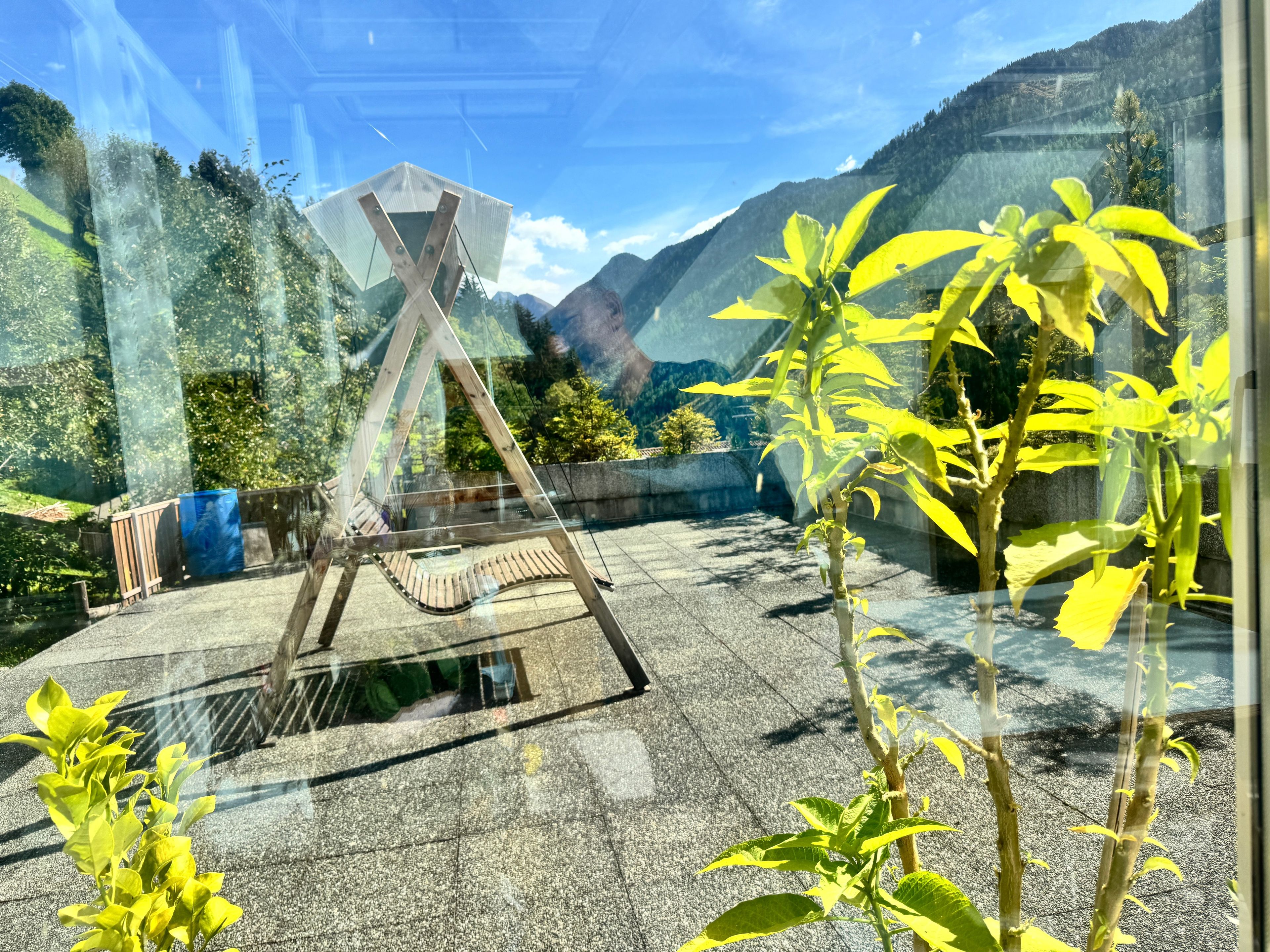 Une pièce dotée d’une grande fenêtre donnant sur un paysage montagneux, d’une balançoire en bois et d’un tonneau bleu.
