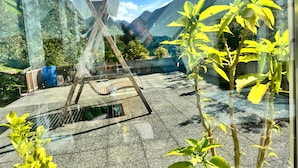 A room with a large window overlooking a mountainous landscape, a wooden swing, and a blue barrel. - Apartment '1' with Mountain View, Shared Garden and Wi-Fi (Selva dei Molini)
