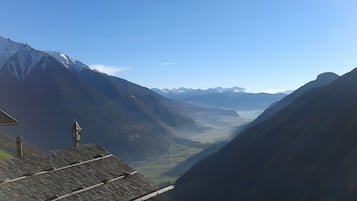 Eine Berglandschaft mit einem Tal, einem Gebäude mit Satteldach und einem Glockenturm.